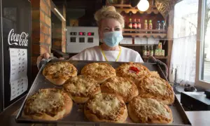 Kobieta w maseczce prezentuje blachę z pizzami. To może być najstarsza pizzeria w Polsce, gdzie tradycja pieczenia pizzy trwa od lat.