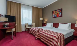 Pokój w hotelu Premier Kraków z dwoma wygodnymi łóżkami, biurkiem i kolorowym obrazem na ścianie.