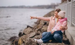 Mama z córką siedzą na kamieniach nad jeziorem. Mama wskazuje coś palcem, a dziewczynka się śmieje. To świetne gąski atrakcje dla dzieci!