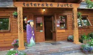 Drewniana fasada z napisem "tatarska jurta" i kolorową figurą w stroju. Zaprasza do środka.