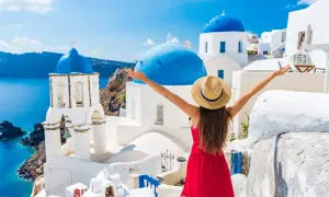 Santorini w kwietniu zachwyca! Kobieta w czerwonej sukience i kapeluszu cieszy się idealną pogodą, podziwiając białe domy i niebieskie kopuły.