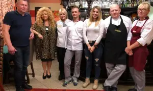 Grupa osób pozuje do zdjęcia w restauracji. Wszyscy wyglądają na zadowolonych, jakby mieli zamiar przyjemnie podjadać.