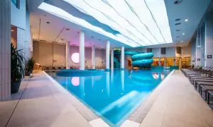 Basen z atrakcjami wodnymi w hotelu Gołębiewski Wisła. Błękitna woda, zjeżdżalnie i nowoczesny sufit.