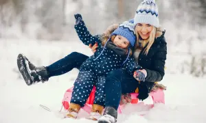 Szczęśliwe ferie świętokrzyskie: mama i córka na sankach w śnieżnym krajobrazie.
