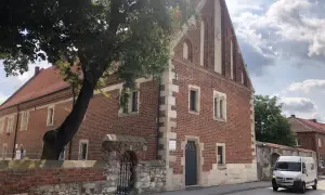 Kamienica z cegły, ozdobiona kamiennymi detalami, to jedna z kazimierza wielka atrakcje. Obok rośnie stare drzewo.