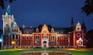 Pałac w Pławniowicach nocą, z oświetloną fasadą i wieżą zegarową. Wspaniałe pławniowice atrakcje czekają na zwiedzających.