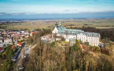Góra Świętej Anny z klasztorem i otaczającą wioską, rozciągająca się na tle pól i błękitnego nieba.