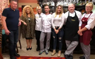 Grupa osób pozuje do zdjęcia w restauracji. Wszyscy wyglądają na zadowolonych, jakby mieli zamiar przyjemnie podjadać.