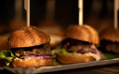 Mini burgery z sałatą, cebulą i ogórkiem na tacy. Idealne do pastelowa menu.