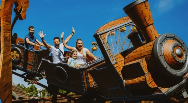 Rodzina krzyczy z radości na pokładzie największego rollercoastera w Polsce, który wygląda jak drewniany pociąg.