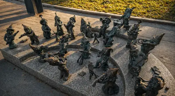 Wrocławskie krasnale, muzycy z brązu, grają na instrumentach na kamiennym postumencie.