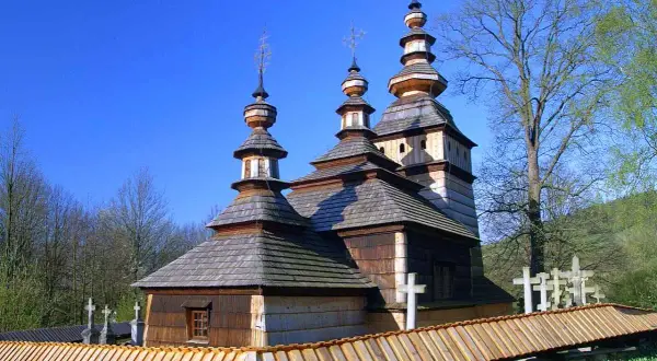 Drewniana cerkiew z trzema kopułami, otoczona drewnianym płotem i krzyżami. Wspaniałe wapienne atrakcje w otoczeniu zieleni.