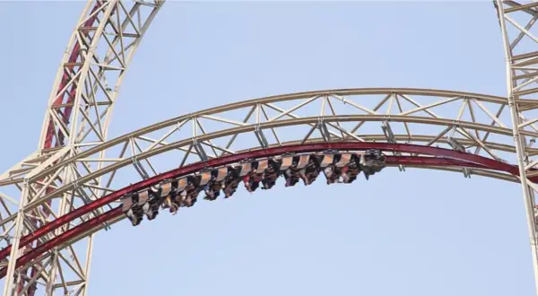 Wagoniki rollercoaster w Polsce pędzą po czerwonym torze na tle błękitnego nieba.