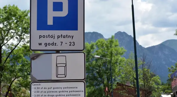 Znaki parkingowe w Zakopanem, informujące o płatnym postoju i cenniku. W tle góry i drzewa, idealne na trasę do skoczni.
