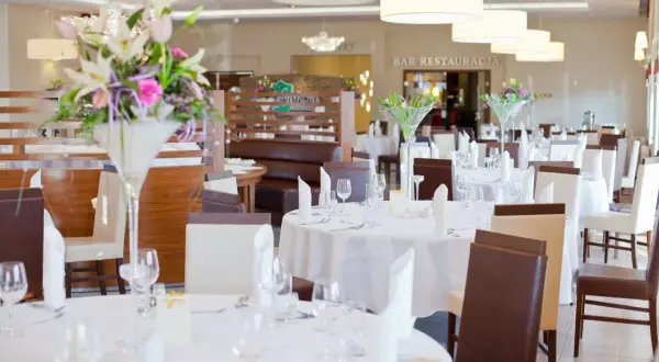 Elegancka sala bankietowa w austerii niemczańskiej, nakryte stoły z kwiatami i białymi obrusami, gotowe na przyjęcie gości.