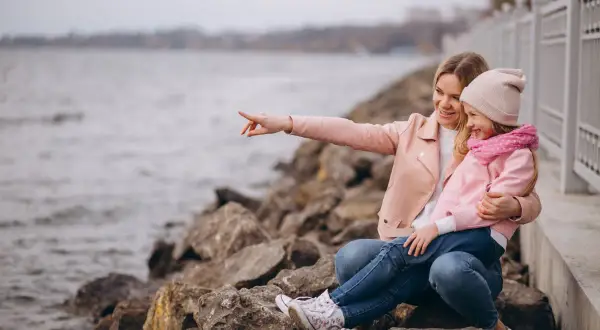 Mama z córką siedzą na kamieniach nad jeziorem. Mama wskazuje coś palcem, a dziewczynka się śmieje. To świetne gąski atrakcje dla dzieci!