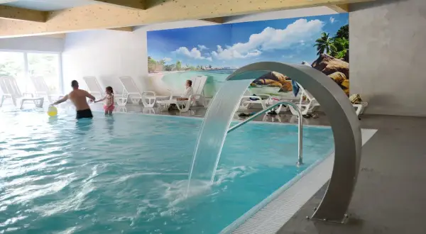 Rodzina bawi się w basenie z wodospadem w hotelu Pokrzywna. Relaks w gorzelnianym klimacie.