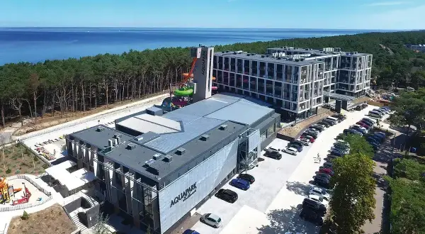 Nowoczesny aquapark i hotel nad morzem, idealne na tanie miejscowości nad morzem. Widać zjeżdżalnie, baseny i parking.
