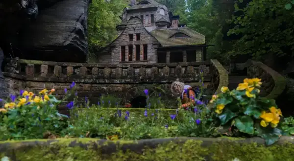 Kamienny domek w lesie, idealne miejsce na nocleg w Czeskiej Szwajcarii. Kwiaty i skalne ściany tworzą magiczny krajobraz.