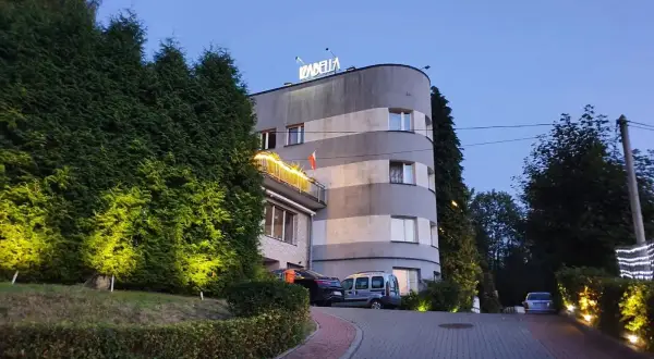 Elegancki hotel Izabella w Puławach, otoczony zielenią i oświetlony wieczorem. Zaprasza do odpoczynku.