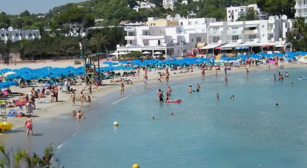 Lloret de Mar, lipiec: słoneczna pogoda zachęca do plażowania. Tłumy ludzi kąpią się i opalają na piaszczystej plaży, pod błękitnymi parasolami.