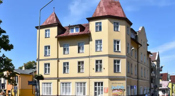 Żółta kamienica w Międzyzdrojach, z banerem "Delfin Międzyzdroje Cennik" i reklamą "Delfin Domowe Obiady".