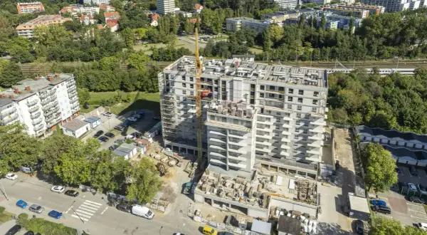 Budowa nowoczesnych, prywatnych mieszkań do wynajęcia nad morzem. Widok z lotu ptaka na osiedle w trakcie realizacji, z dźwigiem budowlanym i widokiem na morze w tle.