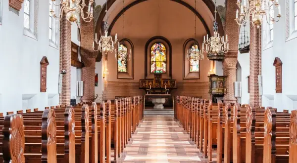 Wnętrze świątyni protestanckiej z rzędami drewnianych ławek, witrażami i ozdobnymi żyrandolami.