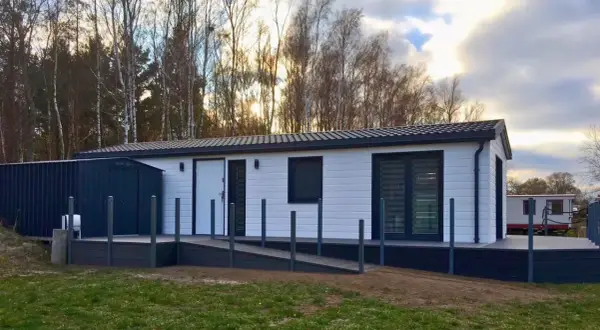 Nowoczesne domki letniskowe przystosowane dla osób niepełnosprawnych, z podjazdem i tarasem, otoczone drzewami.