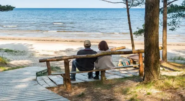 Para relaksu nad morzem, para siedzi na ławce, patrząc na fale. Idealne miejsce na wypoczynek w sanatoriach nad morzem.