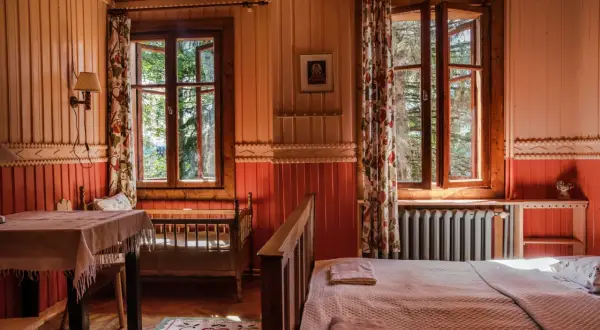 Przytulny pokój z widokiem na leśny ogród Lanckorona. Drewniane ściany, łóżko i stół tworzą sielski klimat.