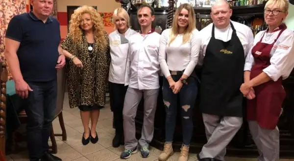 Grupa osób pozuje do zdjęcia w restauracji. Wszyscy wyglądają na zadowolonych, jakby mieli zamiar przyjemnie podjadać.
