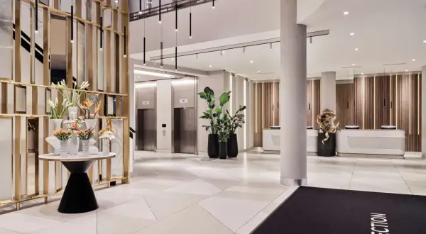 Eleganckie lobby hotelu Radisson Collection Hotel Warsaw z nowoczesnymi windami, recepcją i dekoracjami roślinnymi.