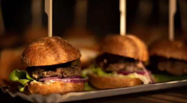 Mini burgery z sałatą, cebulą i ogórkiem na tacy. Idealne do pastelowa menu.
