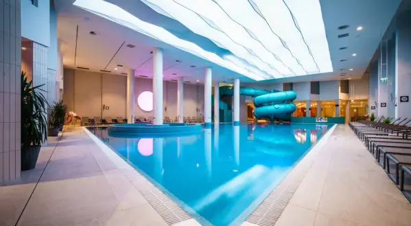 Basen z atrakcjami wodnymi w hotelu Gołębiewski Wisła. Błękitna woda, zjeżdżalnie i nowoczesny sufit.