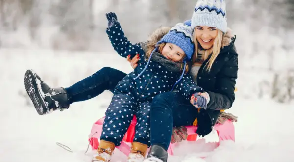 Szczęśliwe ferie świętokrzyskie: mama i córka na sankach w śnieżnym krajobrazie.