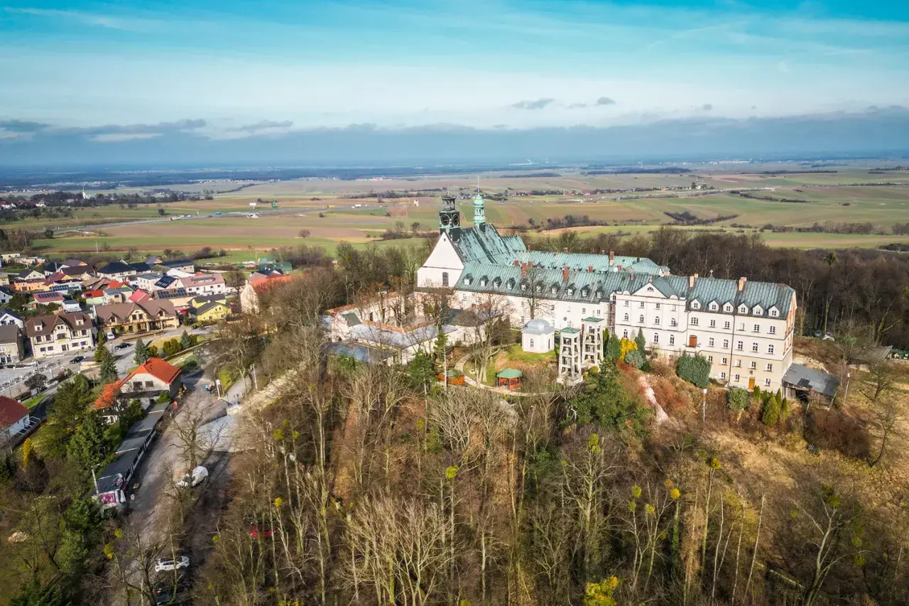 Góra Świętej Anny z klasztorem i otaczającą wioską, rozciągająca się na tle pól i błękitnego nieba.