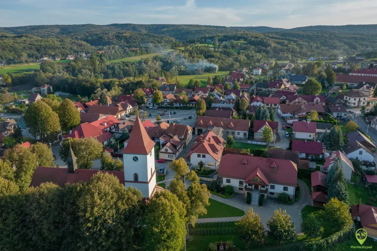 Widok z lotu ptaka na Lipnicę Murowaną. Widać kościół z wieżą, domy z czerwonymi dachami i otaczające lasy. To piękne miejsce oferuje wiele atrakcji.