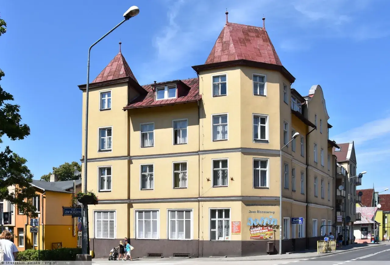 Żółta kamienica w Międzyzdrojach, z banerem "Delfin Międzyzdroje Cennik" i reklamą "Delfin Domowe Obiady".