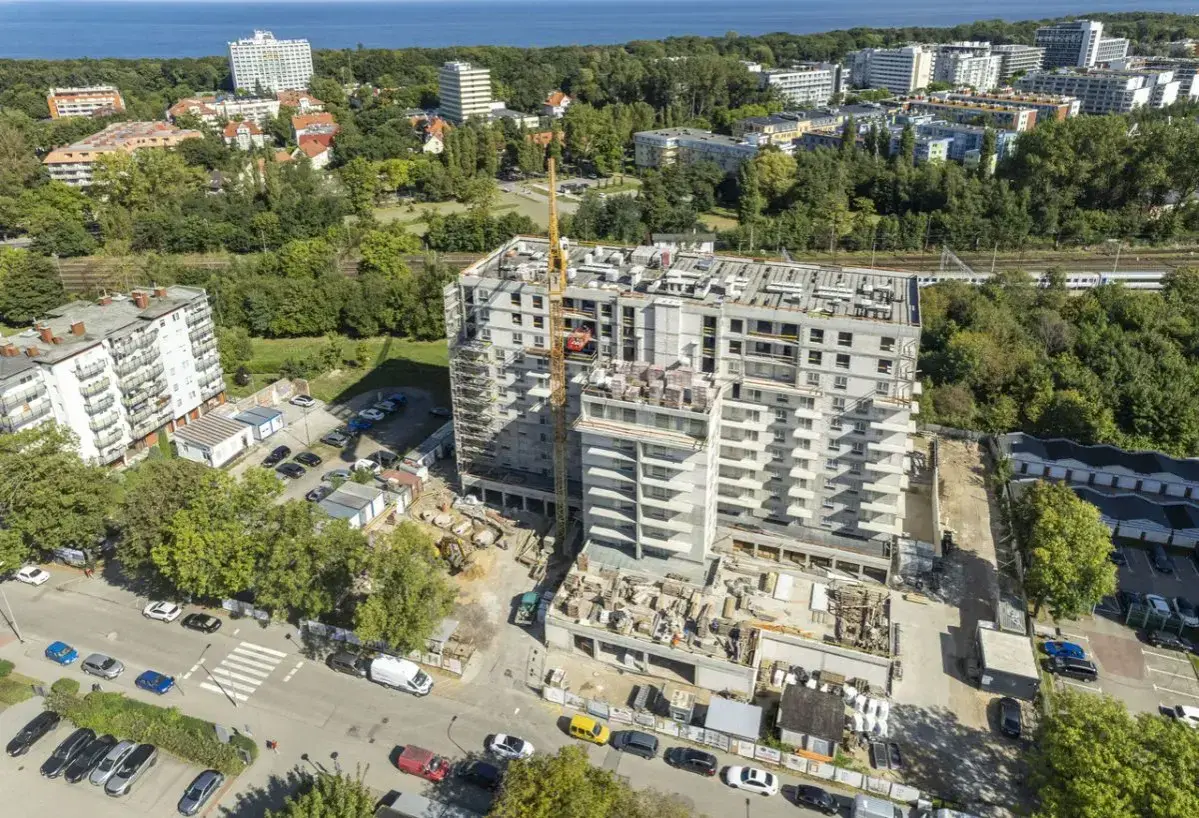 Budowa nowoczesnych, prywatnych mieszkań do wynajęcia nad morzem. Widok z lotu ptaka na osiedle w trakcie realizacji, z dźwigiem budowlanym i widokiem na morze w tle.