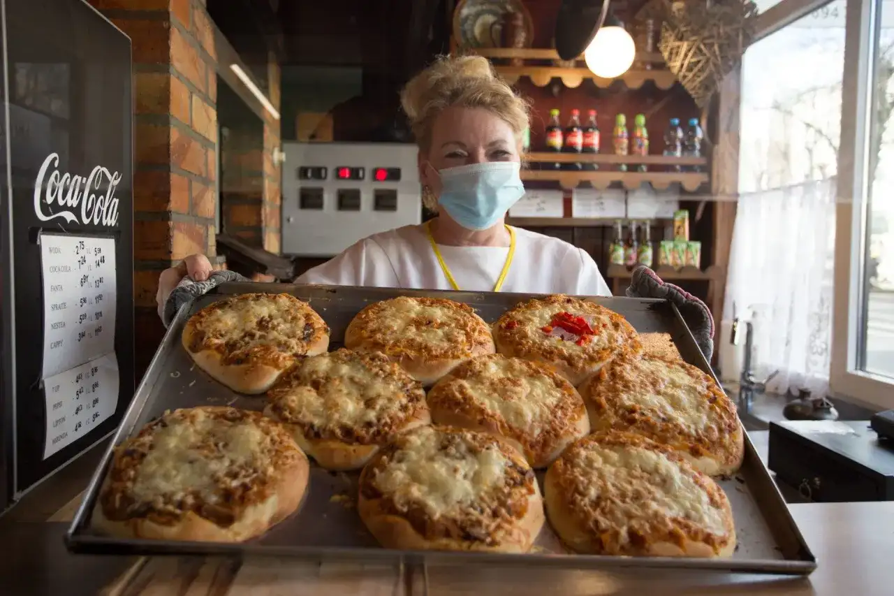 Kobieta w maseczce prezentuje blachę z pizzami. To może być najstarsza pizzeria w Polsce, gdzie tradycja pieczenia pizzy trwa od lat.
