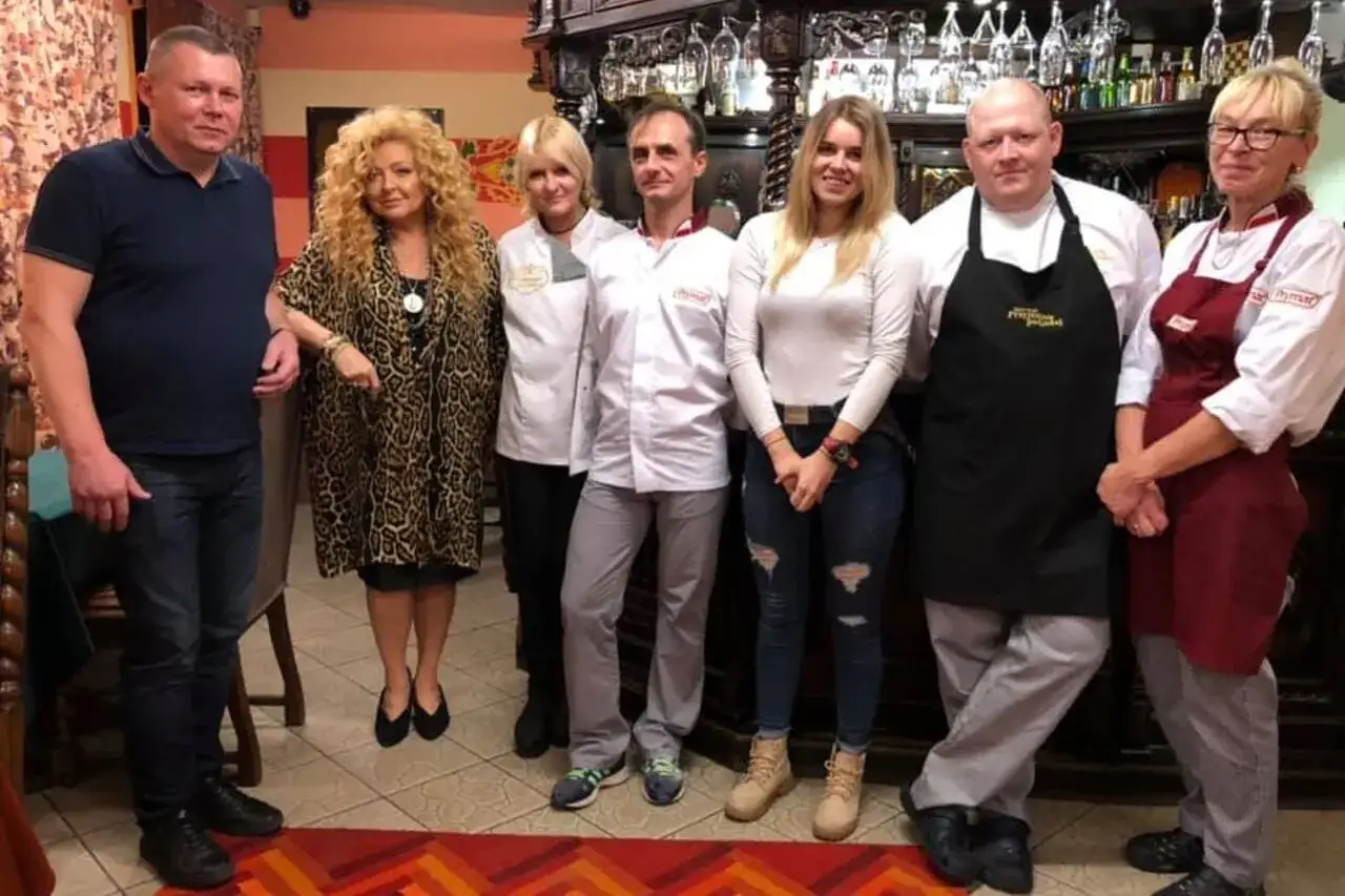 Grupa osób pozuje do zdjęcia w restauracji. Wszyscy wyglądają na zadowolonych, jakby mieli zamiar przyjemnie podjadać.