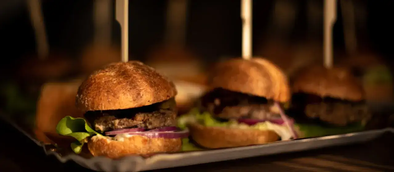 Mini burgery z sałatą, cebulą i ogórkiem na tacy. Idealne do pastelowa menu.