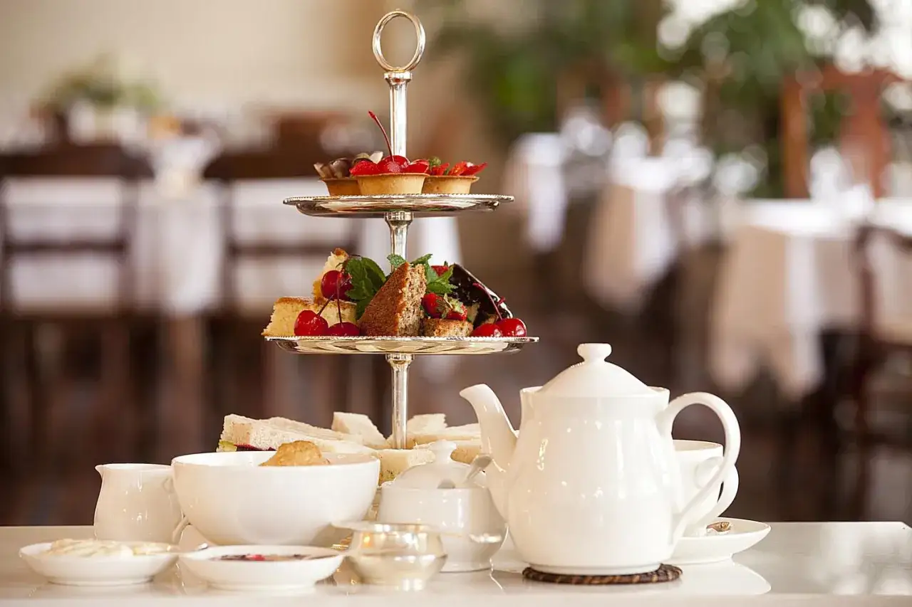 Elegancki zestaw do tea time: piętrowa etażerka z ciastkami i owocami, kanapki, czajniczek i porcelana.