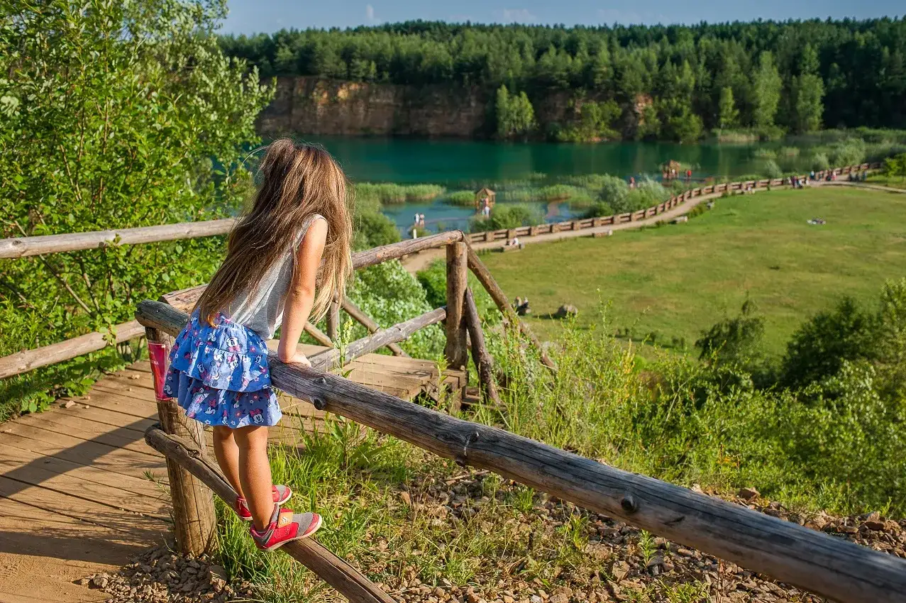 Dziewczynka na drewnianej kładce podziwia zalew w Jaworznie. Park Gródek Jaworzno cena wstępu jest przystępna dla rodzin.