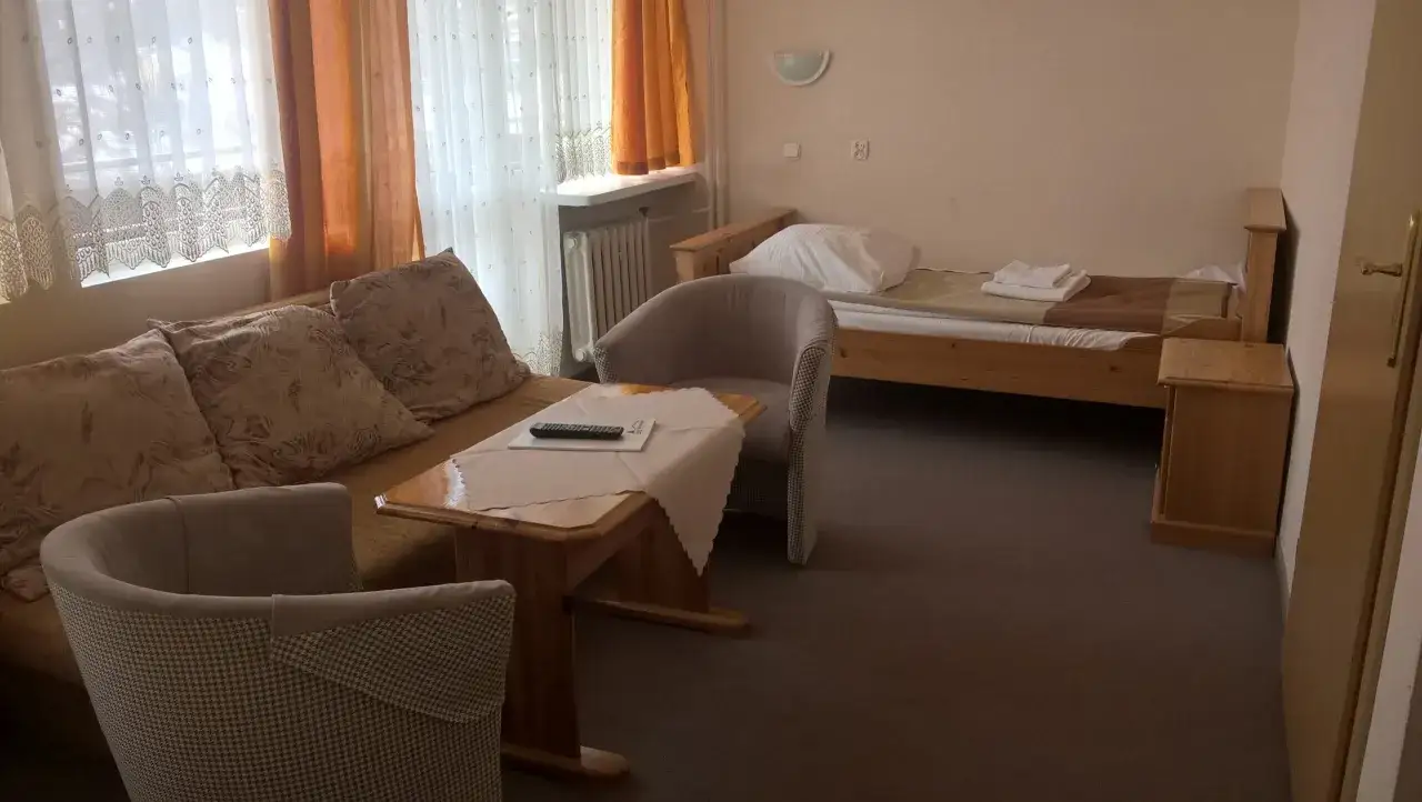 Pokój w sanatorium uzdrowiskowym „Leśnik”. Wygodna kanapa, stolik kawowy, fotel i łóżko z pościelą.