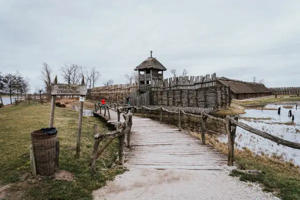 Drewniany mostek prowadzi do grodziska z wieżą strażniczą i zabudowaniami, część szlaku piastowskiego.