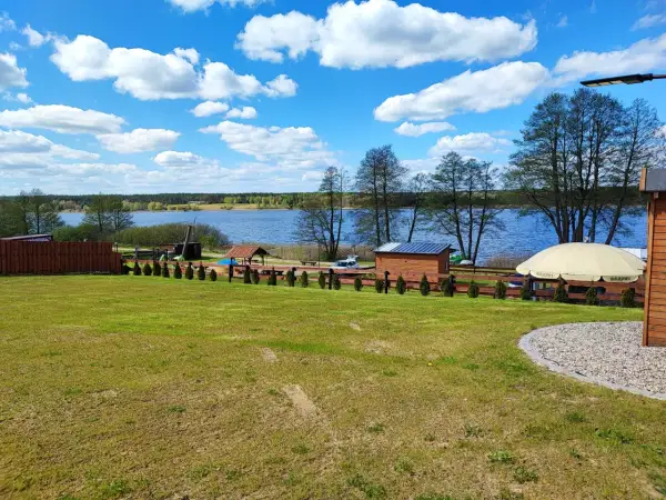 Piękny dzień nad jeziorem skarlińskim. Błękitne niebo z białymi chmurami, zielona trawa i spokojna tafla wody.