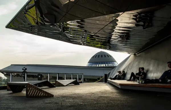 Nowoczesna architektura i nietypowe atrakcje Katowice. Ludzie odpoczywają pod futurystycznym zadaszeniem, w tle kopuła Muzeum Śląskiego.