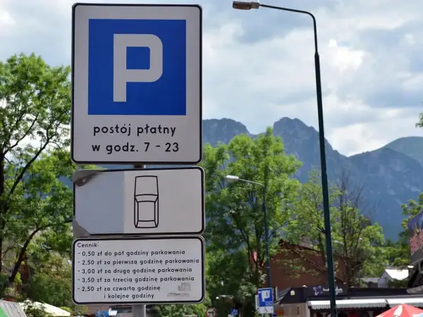 Znaki parkingowe w Zakopanem, informujące o płatnym postoju i cenniku. W tle góry i drzewa, idealne na trasę do skoczni.